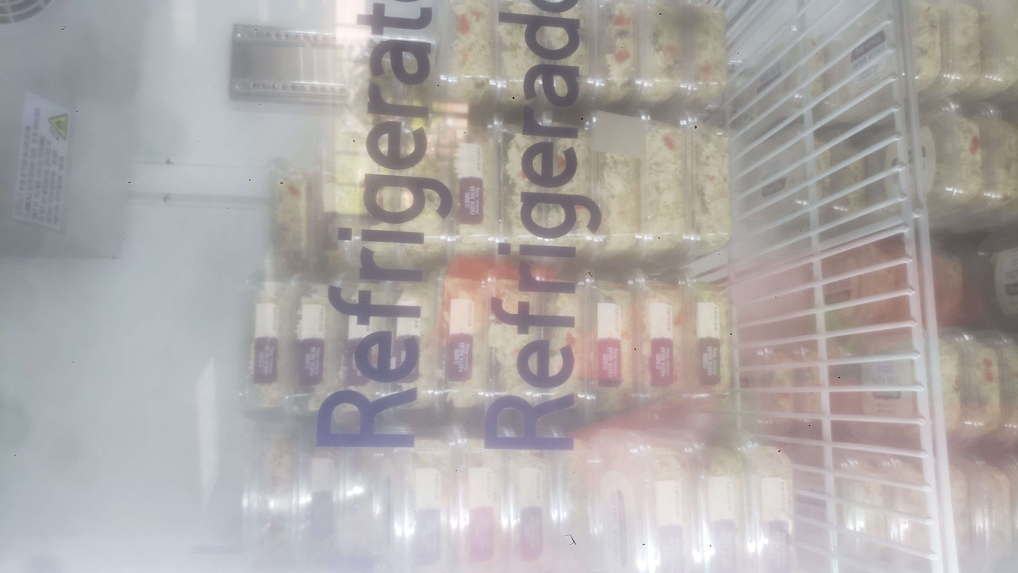 Containers of pasta salad on the shelves of a fridge